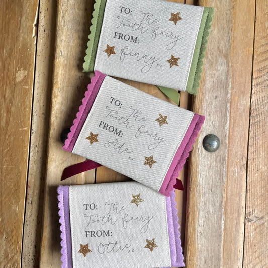Decorative tooth fairy pouch with personalised text and star designs on a wooden surface in green, purple and lilac