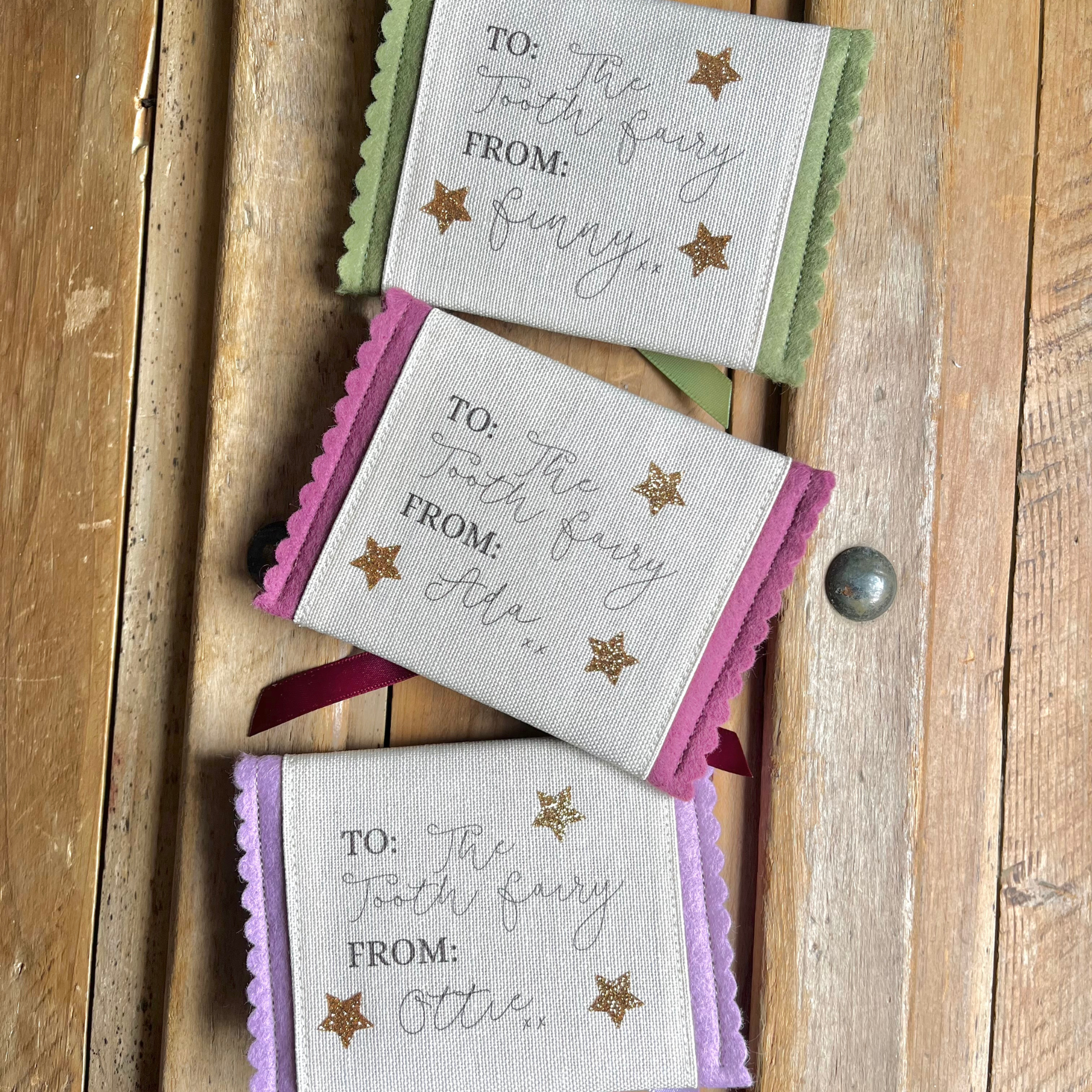 Decorative tooth fairy pouch with personalised text and star designs on a wooden surface in green, purple and lilac