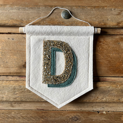 Cream felt initial banner with chunky gold glitter and teal drop shadow effect perfect for kids room decor