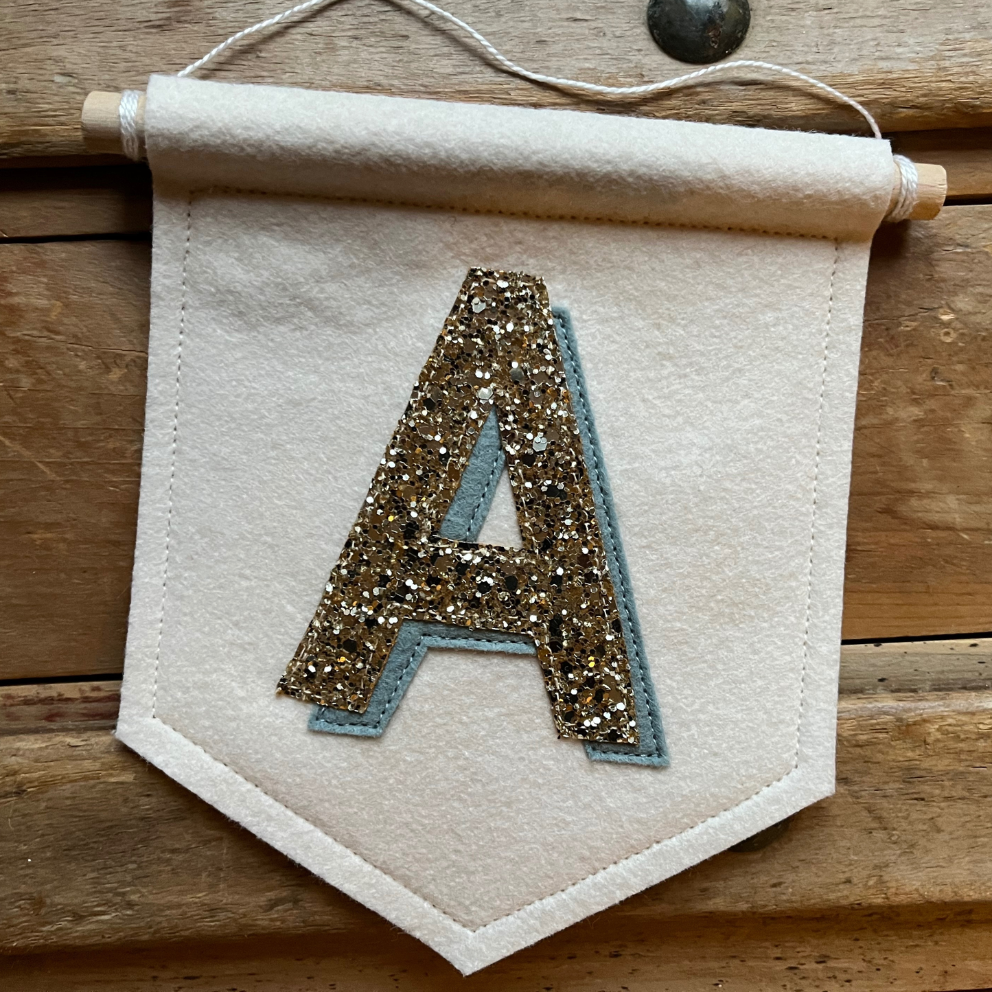 Cream felt initial banner with chunky gold glitter and powder blue drop shadow effect perfect for kids room decor