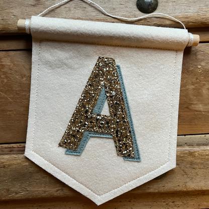 Cream felt initial banner with chunky gold glitter and powder blue drop shadow effect perfect for kids room decor