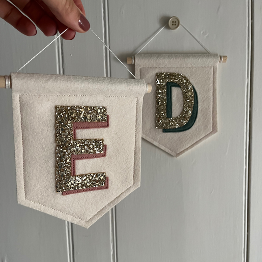 Two personalised initial wall pennants displayed, one hanging on door and the other being held to show perfect for kids room decor.